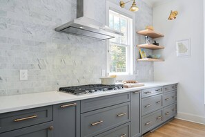A kitchen with grey cabinets, a white countertop, and a stove. There are wooden shelves on the wall and a window above the counter. - Adair Say (Atlanta)