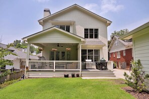 A two-story house with a covered porch, a chimney, and a small backyard with a lawn and potted plants.