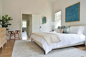 A bedroom with a bed, a bedside table, a lamp, a mirror, and a painting.