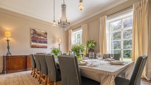 Ein Esszimmer mit einem großen Tisch, gedeckt für sechs Personen, umgeben von sechs Stühlen, einer Deckenleuchte und einem Fenster mit Vorhängen.