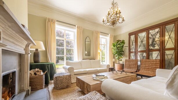 Ein gemütliches Wohnzimmer mit Kamin, weißen Sofas, einem Holztisch und einem großen Fenster mit Vorhängen.