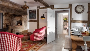 Une pièce chaleureuse avec des murs en briques apparentes, une cheminée, un fauteuil à motifs à carreaux, une table à manger avec des chaises et une horloge au mur.