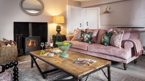 Un salon chaleureux avec une cheminée, un canapé rose, une table basse en bois et un panier en osier.