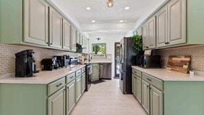 A modern kitchen with light green cabinets, a central island, and a view of the outside. - Family-Friendly Gainesville Home - Walk to UF - Pool + Sleeps 16 (Gainesville)