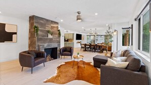 A modern living room with a fireplace, leather sofas, a dining area, and large windows. - Family-Friendly Gainesville Home - Walk to UF - Pool + Sleeps 16 (Gainesville)