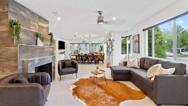 A modern living room with a fireplace, leather sofas, a cowhide rug, and a dining area in the background. - Family-Friendly Gainesville Home - Walk to UF - Pool + Sleeps 16 (Gainesville)