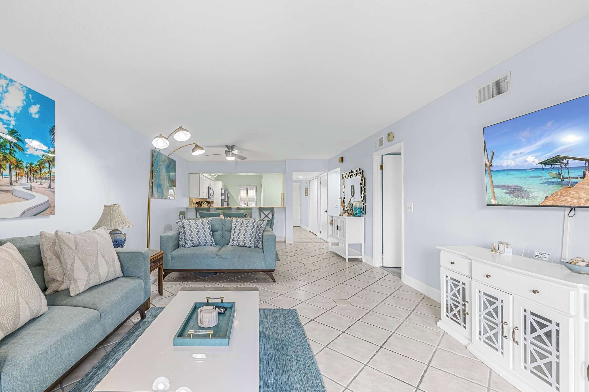 A living room with a sofa, coffee table, and TV. There is a hallway leading to a bedroom with a door.