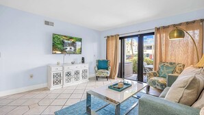 Ein Wohnzimmer mit Fernseher, einer Couch, einem Sessel, einem Couchtisch und Blick ins Freie.