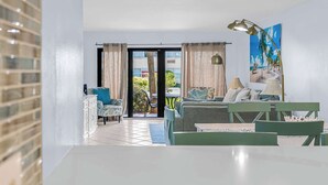 Ein modernes Wohnzimmer mit einer Couch, Stühlen, einem Esstisch und Blick ins Freie durch eine Glastür.