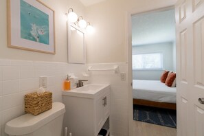 Une salle de bain avec des toilettes, un lavabo et un miroir, et une chambre avec un lit et une fenêtre.