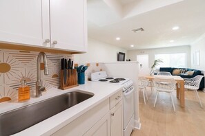 A modern kitchen with white cabinets, a stainless steel sink, and a dining area with white chairs and a wooden table.