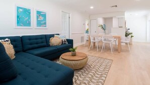 A modern living room with a sectional sofa, a round coffee table, and a dining area with white chairs. - Beachside 2BR Retreat in Cocoa Beach (Cocoa Beach)