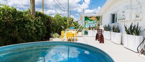 A swimming pool with a patio area, a building with a sign reading 'KEEP IT SHINY,' and potted plants.