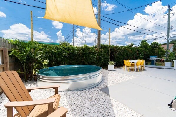 Ein Garten mit Whirlpool, einem Holzstuhl, einem Tisch mit gelben Stühlen und einem gelben Sonnensegel.