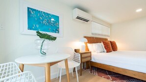 A bedroom with a bed, bedside table, lamp, and a wall-mounted air conditioner. - THE JUNI Studio Surf Paradise in Heart of Cocoa Be (Cocoa Beach)