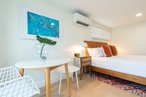 A bedroom with a bed, bedside table, lamp, and a wall-mounted air conditioner.