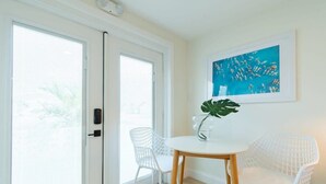 A modern room with a white table and chairs, a large window with blinds, and a framed abstract painting on the wall. - THE JUNI Studio Surf Paradise in Heart of Cocoa Be (Cocoa Beach)