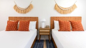 A double room with two beds, each with a wooden headboard, white bedding, and orange patterned pillows. There is a small bedside table with a lamp and a radio between the beds. - Beachside Studio in Cocoa Beach (Cocoa Beach)