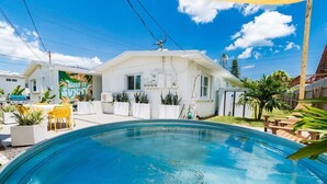A swimming pool with a white house in the background, a patio with chairs, and a 'KEEP IT SUNNY' mural. - Beachside Studio in Cocoa Beach (Cocoa Beach)