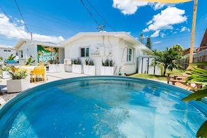 A swimming pool with a white house in the background, a patio with chairs, and a 'KEEP IT SUNNY' mural. - THE JUNI ✺ Stunning Studio, Walk to Everything (Cocoa Beach)