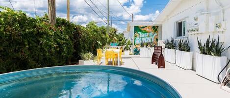 A swimming pool with a patio area, a building with a sign reading 'KEEP IT SHINY,' and potted plants.