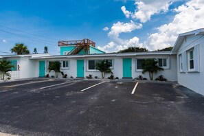 A motel with a parking lot, a staircase to the upper level, and a clear blue sky. - THE JUNI - Studio Steps to Beach, Downtown Cocoa (Cocoa Beach)