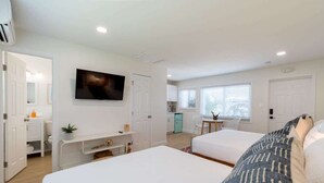 A bedroom with two beds, a TV, a kitchenette, and a bathroom.