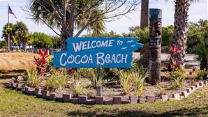 A welcome sign to Cocoa Beach with a tropical garden and a tiki statue.