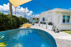 A swimming pool with a sunshade, a small outdoor seating area, and a building with a 'KEEP IT SUMMER' sign. - THE JUNI - Studio Steps to Beach, Downtown Cocoa (Cocoa Beach)