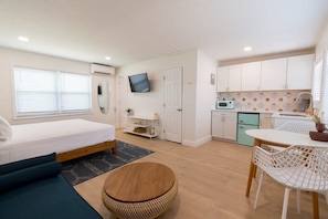 A compact room with a bed, a dining table with chairs, a kitchen area, and a TV mounted on the wall.