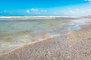 A beach with pebbly shore, clear water, and distant waves.