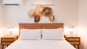 A hotel room with a bed, two bedside tables with lamps, a wall-mounted air conditioner, and a collection of hats hanging on a rack above the bed. - Welcome to The Juni-The Streets (Cocoa Beach)