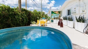A swimming pool with a patio area, a building with a sign reading 'KEEP IT SHINY,' and potted plants. - Welcome to The Juni-The Streets (Cocoa Beach)