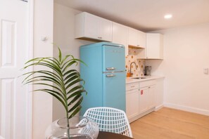 Uma cozinha compacta com armários brancos, uma geladeira azul, uma mesa de jantar com uma cadeira e um vaso de planta.