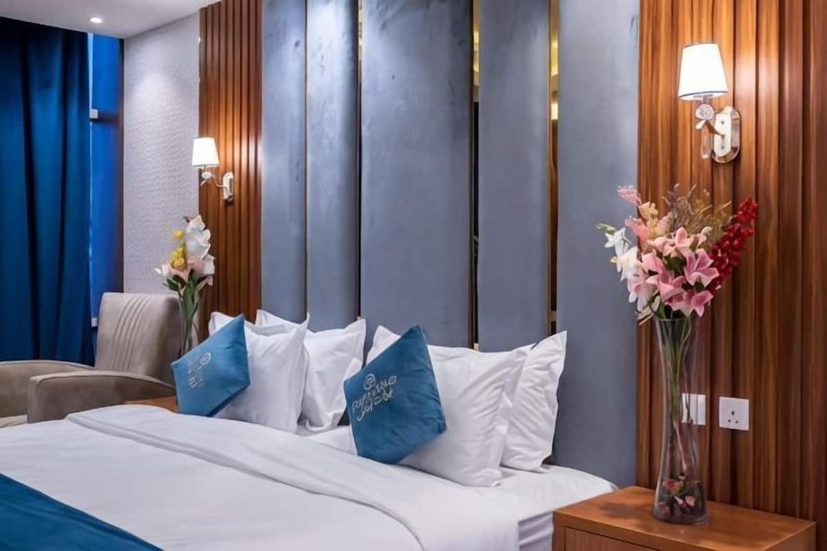 Une chambre d’hôtel avec un lit, une table de chevet, une lampe et un vase de fleurs.