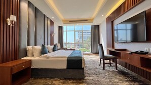 A hotel room with a large bed, a desk, a chair, a TV, and a view of the city. - Paradise Inn Jeddah (Jeddah)