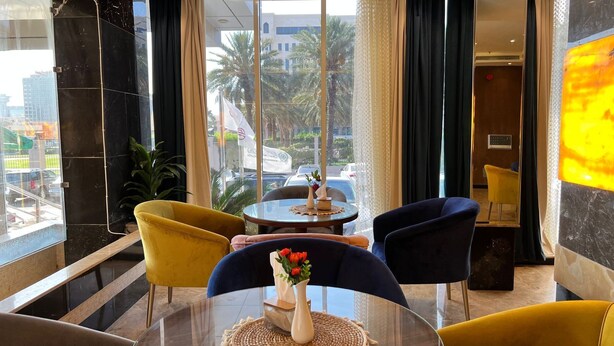 A hotel lobby with a round table, two yellow armchairs, and a blue armchair. A vase with red flowers is on the table. - Paradise Inn Jeddah (Jeddah)