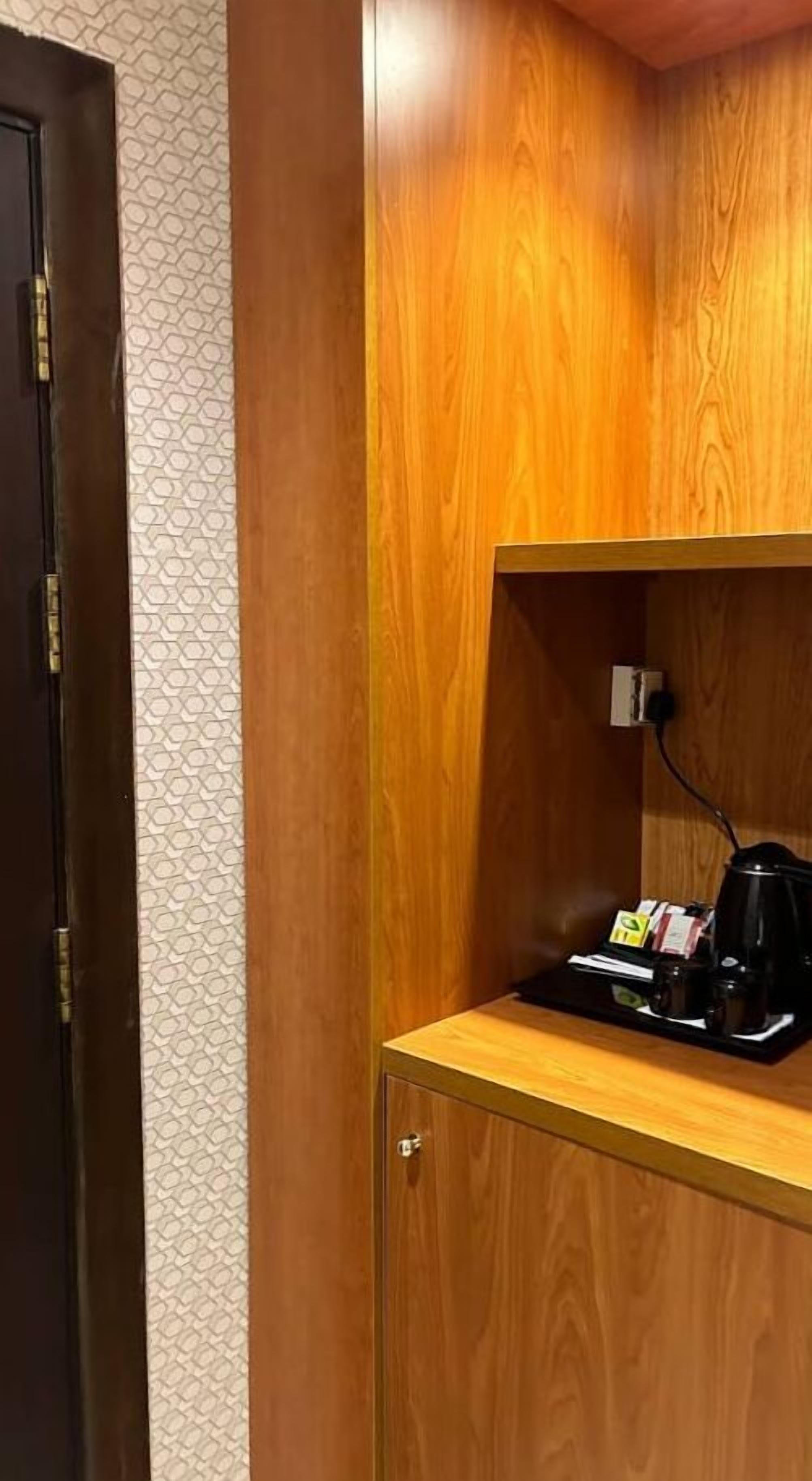 A wooden cabinet with a shelf containing a coffee maker, a kettle, and some items on a tray.