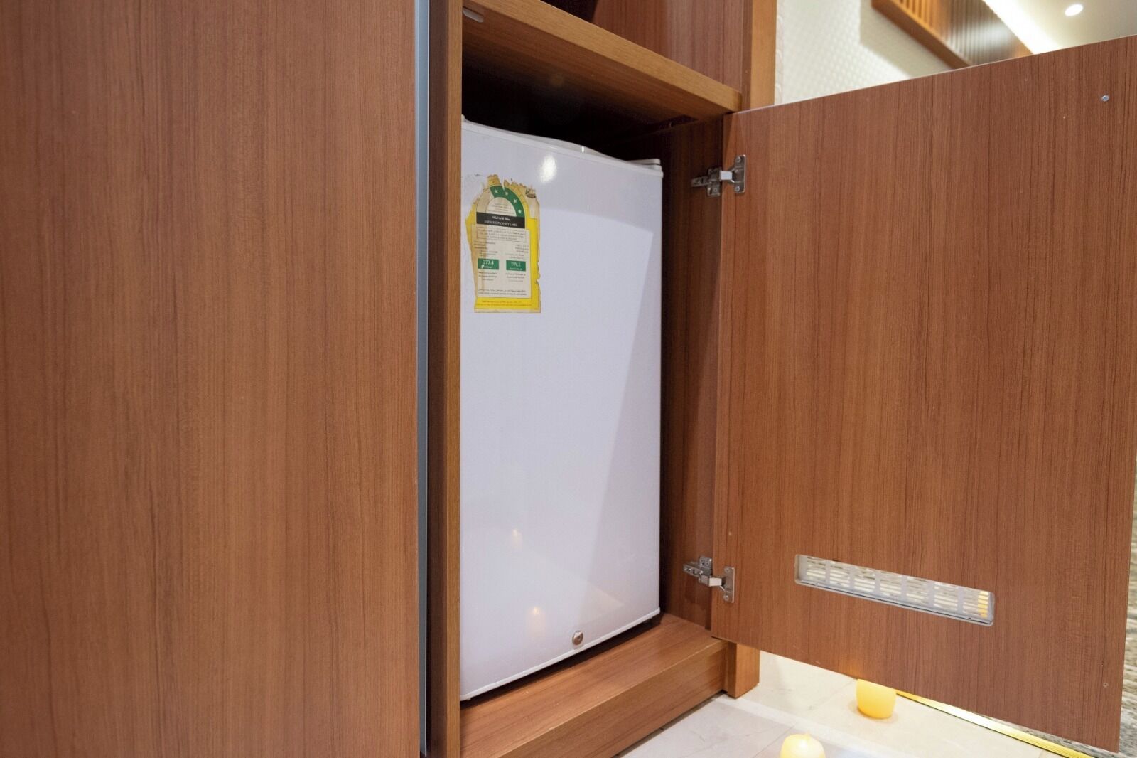 A wooden cabinet with a white appliance inside, a label on the door, and a small yellow object on the floor.