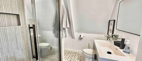 Un baño moderno con cabina de ducha de vidrio, un lavabo blanco y un espejo.