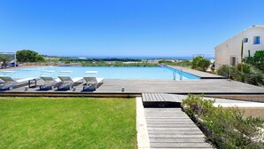 A swimming pool with lounge chairs, a wooden deck, and a view of the sea.