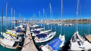 A marina with numerous sailboats docked, a wooden walkway, and a clear blue sky.