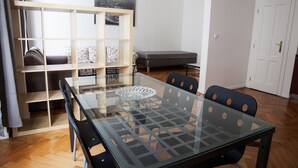 A modern living room with a glass-top dining table, black chairs, a wooden shelving unit, a grey sofa, and a bench. - 2 Bed Flat - Sleeps 9 - Pets - Smoking on Terrace (Prague)