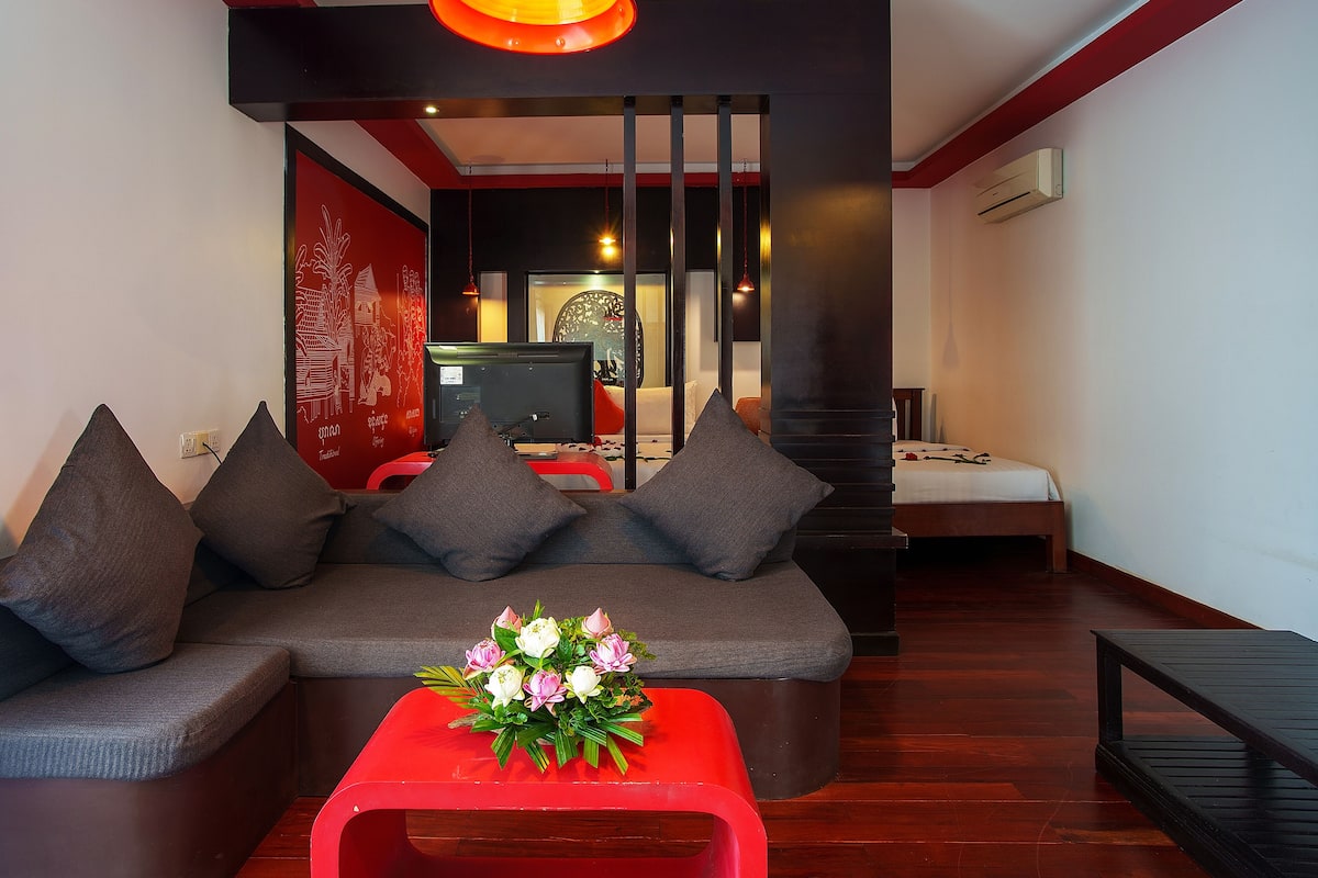 A modern living room with a sofa, red ottoman, and a flower arrangement.