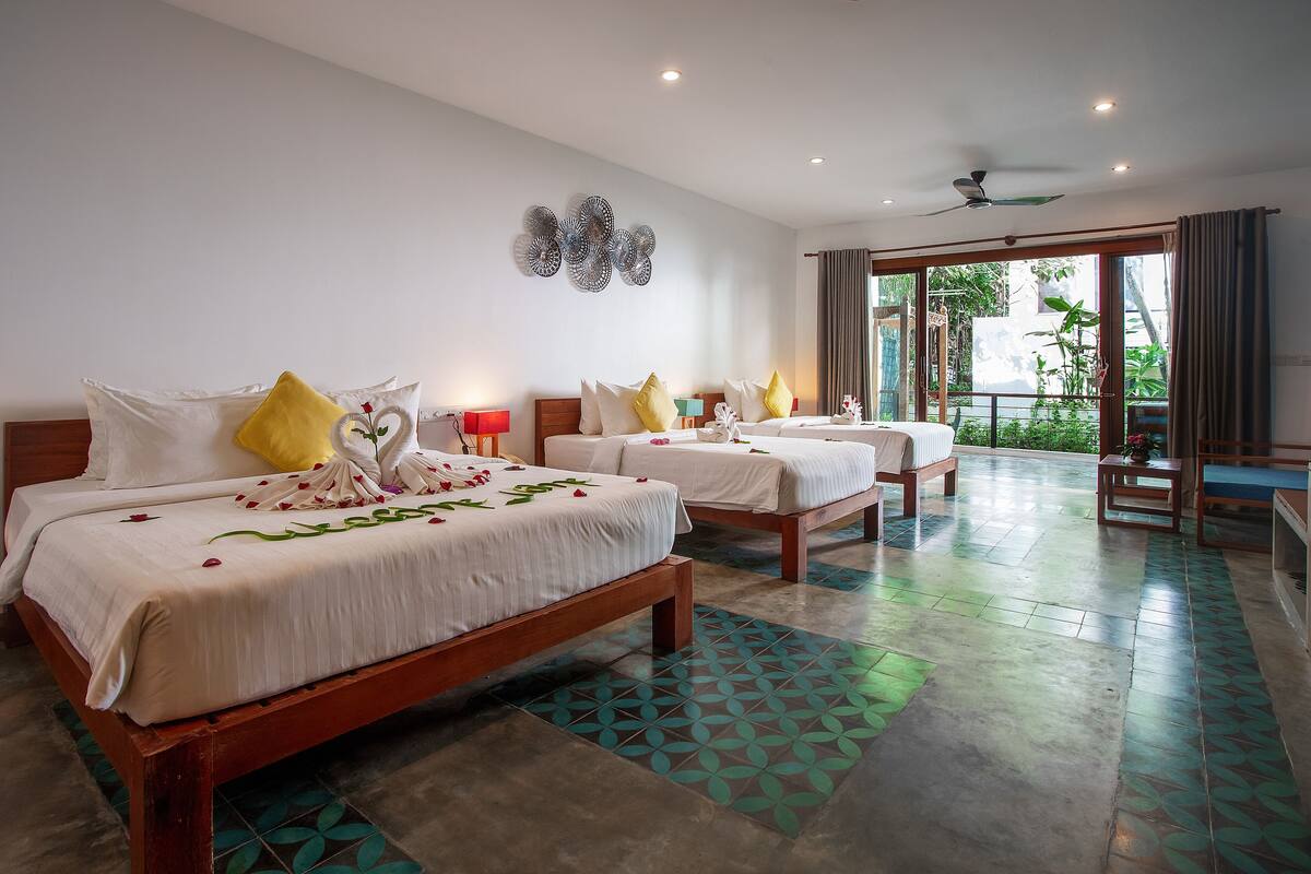 A hotel room with two beds, a balcony, and a view of greenery.