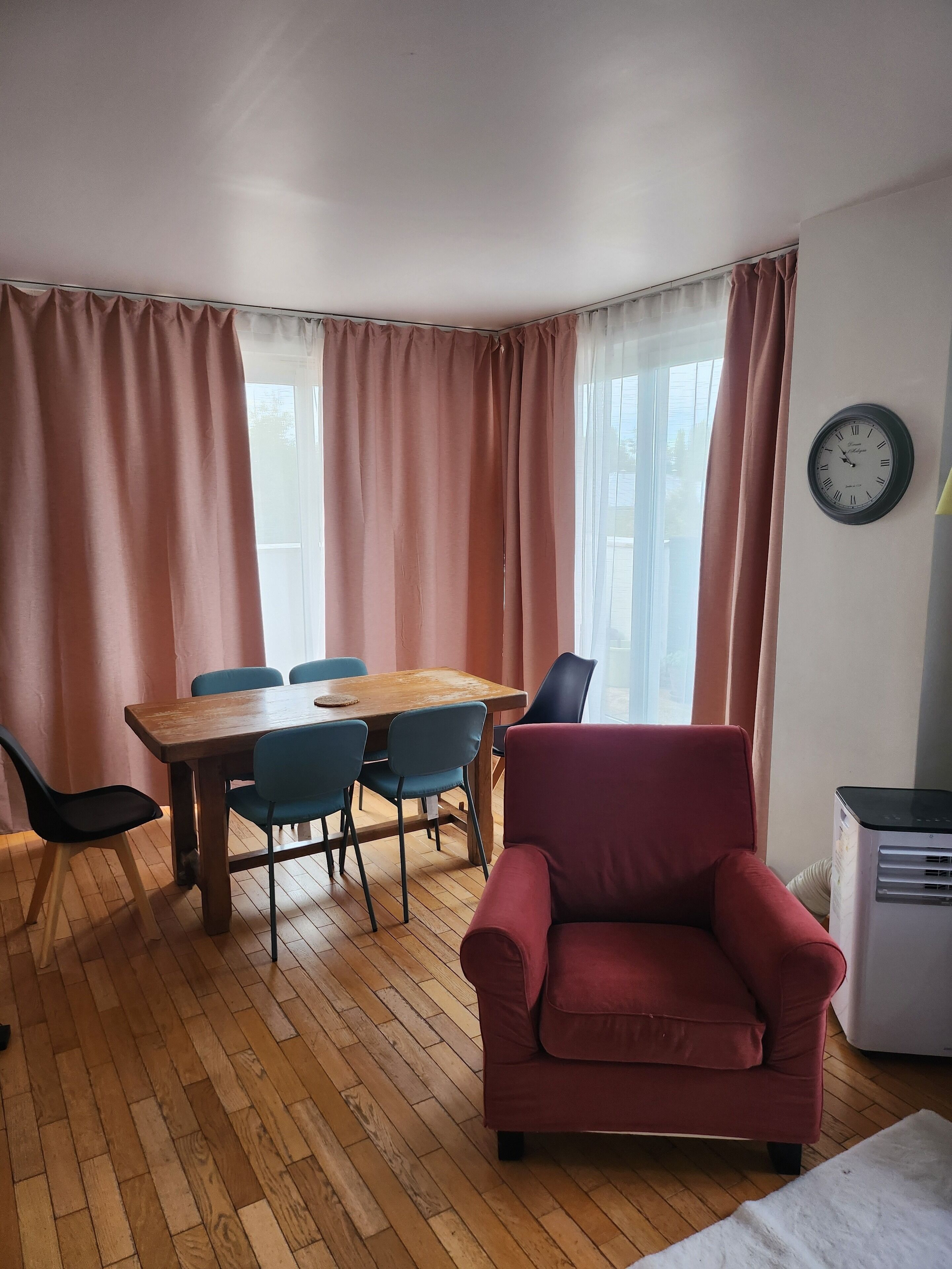 A room with a wooden dining table, blue chairs, a red armchair, and a white radiator.
