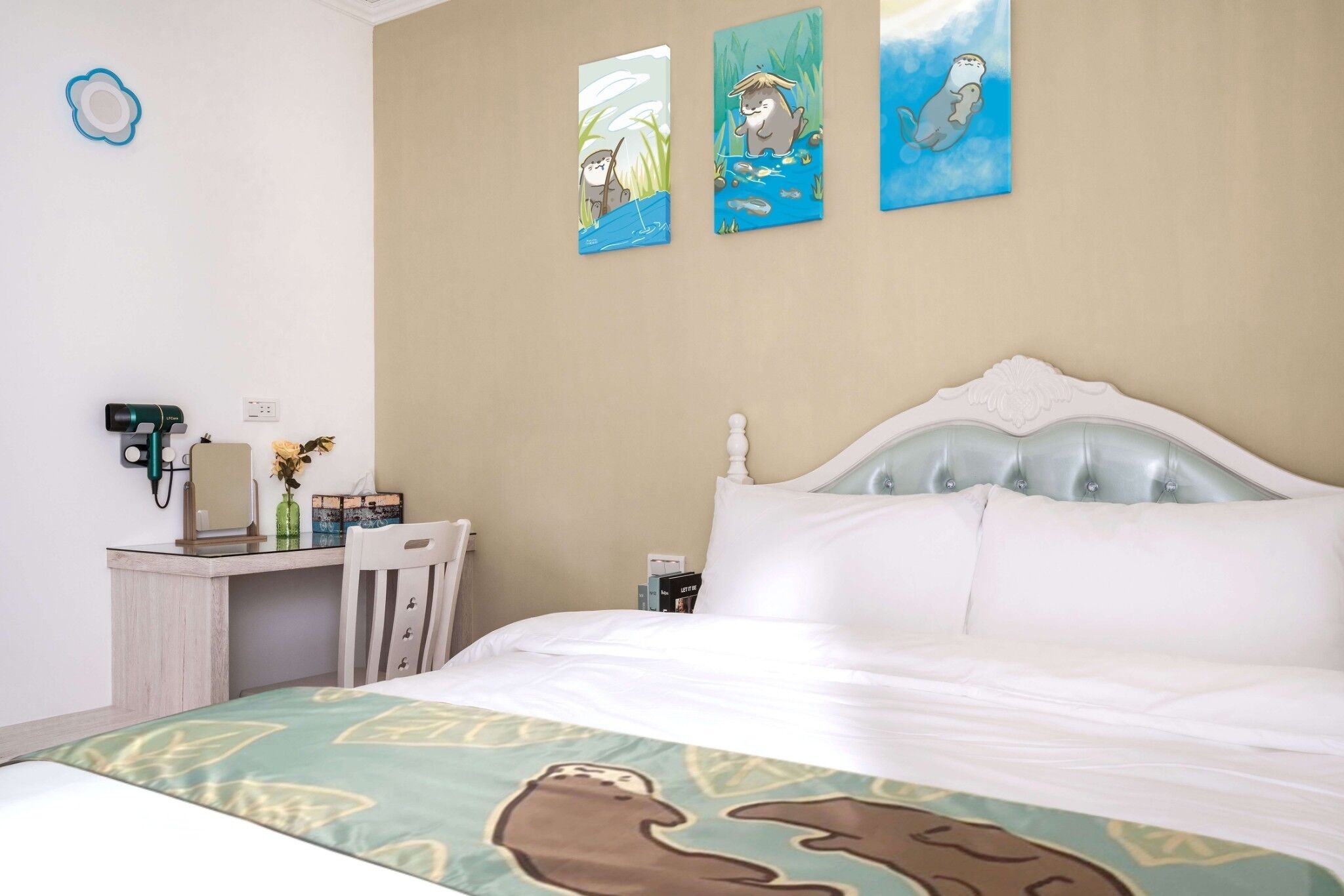Quarto de hotel com uma cama, uma escrivaninha e uma cadeira. Três quadros na parede.