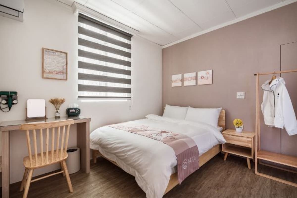 A bedroom with a bed, a desk, a chair, a bedside table, and a wardrobe.