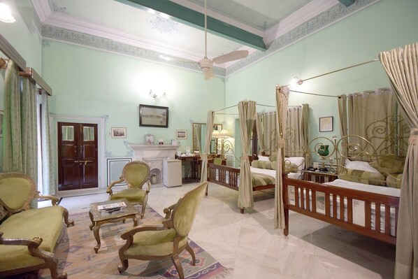 A spacious room with a large bed, a sitting area with chairs, a fireplace, and a ceiling fan. - Hari Mahal Palace-By Pachar Group (Jaipur)