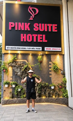 Un letrero del Hotel Pink Suite con un diseño moderno, que incluye un logotipo, dirección y número de teléfono de contacto.